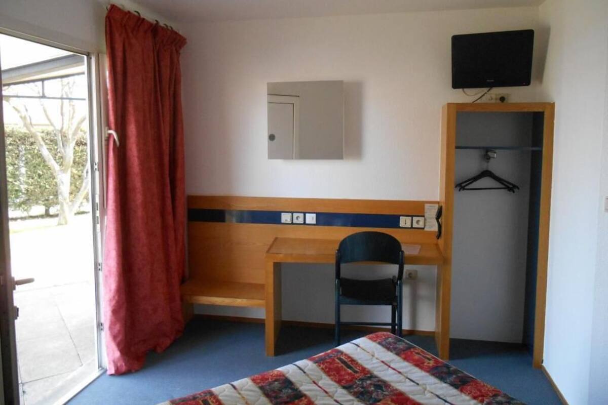 A room with a bed, a desk, a chair, a wardrobe, and a television.