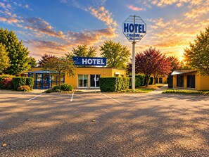 Un hotel con un cartel llamativo, un acceso cubierto y un estacionamiento.