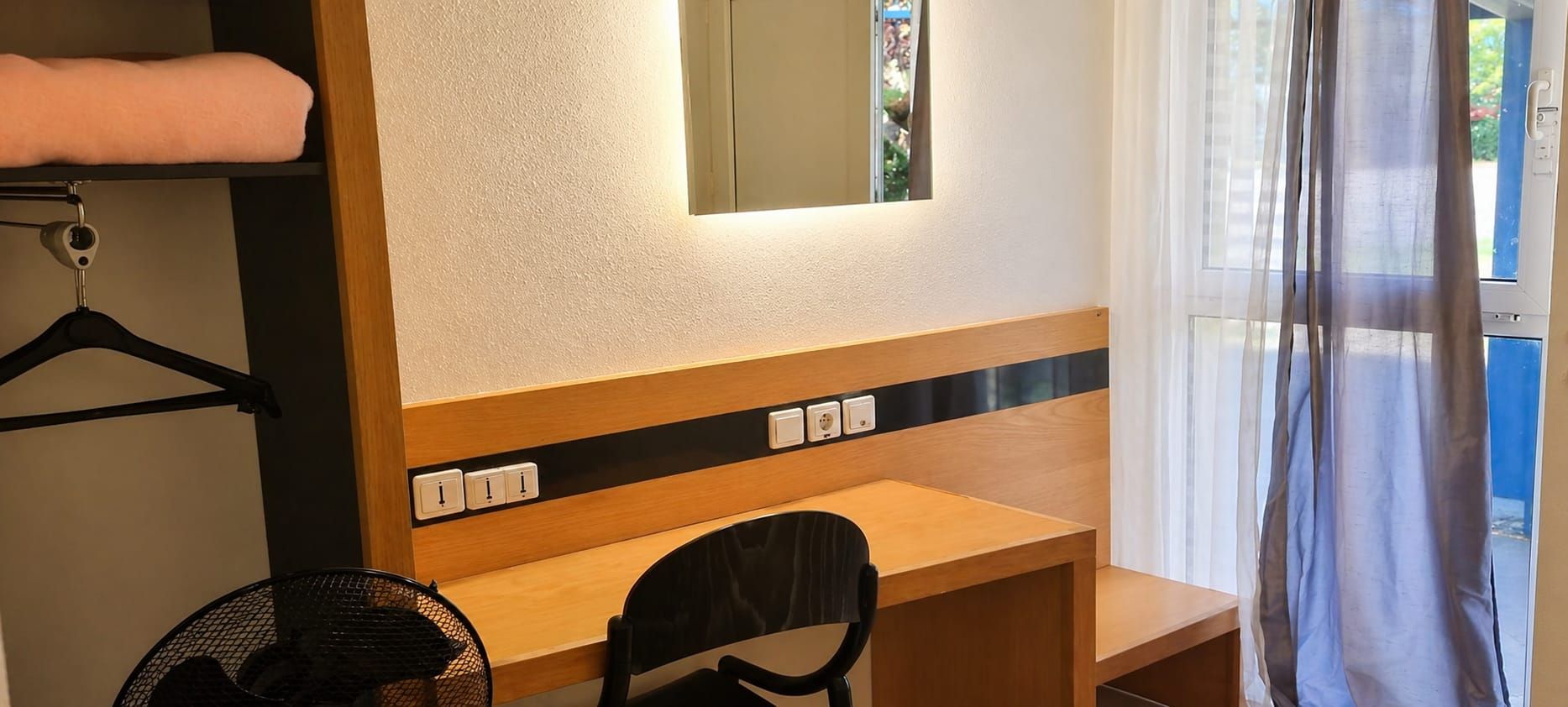 Una habitación con un escritorio de madera, una silla, una toalla colgada y una ventana con cortinas.