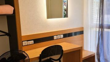 Une pièce avec un bureau en bois, une chaise, une serviette suspendue et une fenêtre avec des rideaux.