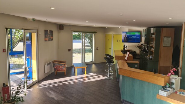 Zona de recepción de un hotel con un mostrador de madera, una pantalla de televisión y un teléfono.