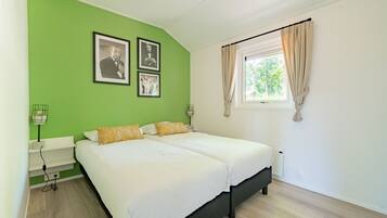 A bedroom with two beds, green walls, and a window with curtains.