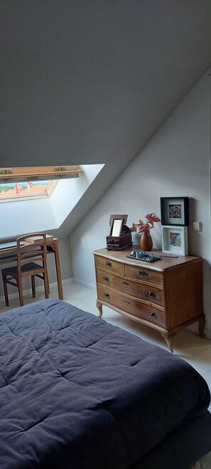 Un dormitorio con techo inclinado, una cama, un aparador, un escritorio y una silla.