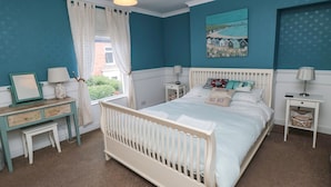 A bedroom with a white crib, a bedside table with a lamp, a dresser, and a window with curtains.