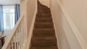 A carpeted staircase with white balusters and a handrail, leading to an upper floor.