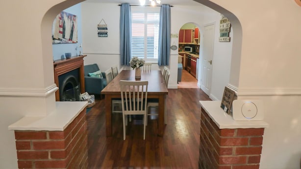A dining area with a wooden table and chairs, a fireplace, and a view into the kitchen.