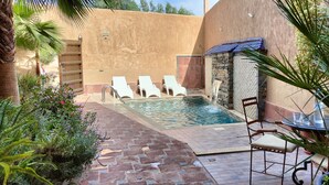 A pool area with lounge chairs, a table, and a stone wall. - DAR ELWALI ROUTE WARZAZT (Chwiter)