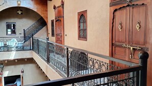 A multi-level interior with a staircase, ornate wooden doors, and a balcony with a wrought iron railing. - DAR ELWALI ROUTE WARZAZT (Chwiter)