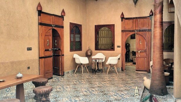 A traditional Moroccan courtyard with wooden doors, tiled flooring, and a small table with chairs. - DAR ELWALI ROUTE WARZAZT (Chwiter)