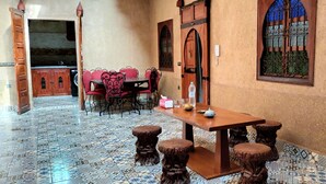 A dining area with a wooden table and chairs, a tiled floor, and a decorative window. - DAR ELWALI ROUTE WARZAZT (Chwiter)