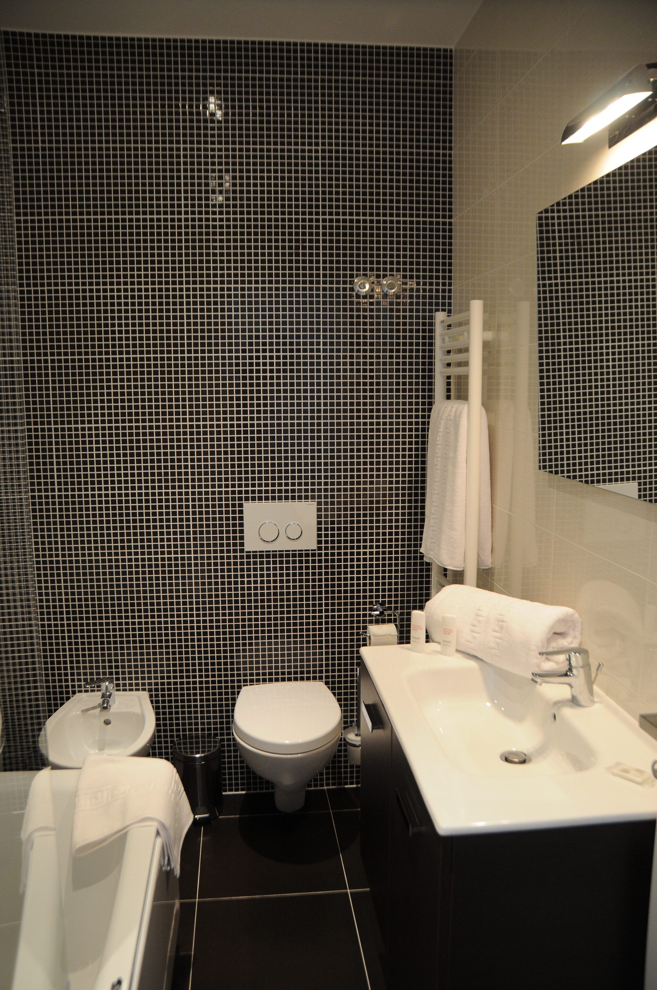 Une salle de bain moderne avec un mur recouvert de carreaux noirs et blancs, un lavabo blanc, des toilettes et une baignoire.