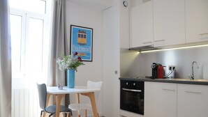 A modern kitchen with white cabinets, a built-in oven, and a coffee maker. There is a dining table with two chairs and a vase with flowers. - Studio luxury Lisbon i (Lisboa)