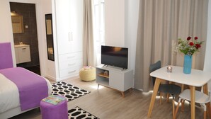 Een moderne hotelkamer met een bed, een televisie, een eettafel en een klein tafeltje met een bloemetjesvaas.