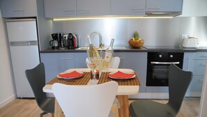 Una cocina moderna con una mesa de comedor lista para dos personas, equipada con cafetera, botellas de vino y un frutero.