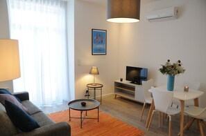 Un salon moderne comprenant un canapé, une petite table ronde, un téléviseur et un coin repas avec des chaises et un vase de fleurs.
