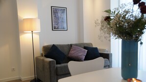 Ein modernes Wohnzimmer mit grauem Sofa, Stehlampe, gerahmtem Kunstwerk und einer Vase mit Blumen.