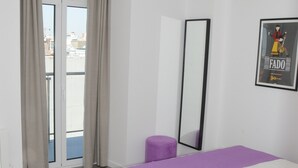 Ein Schlafzimmer mit einem Bett, einem großen Fenster mit Vorhängen, einer Deckenleuchte und einem gerahmten Bild an der Wand.