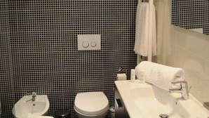 Moderni kylpyhuone, jossa on mustavalkoisesti laatoitettu seinä, valkoinen pesuallas, wc-istuin ja kylpyamme.