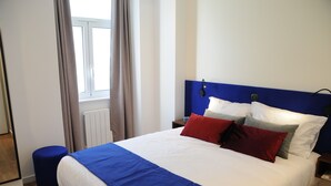 A neatly made bed with a blue headboard, white bedding, and red and grey pillows. - Charming Comfortable Apartment with Balcony 1 (Lisboa)