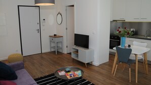 A modern living room with a sofa, coffee table, TV, and a dining area with chairs and a table. - Charming Comfortable Apartment with Balcony 1 (Lisboa)