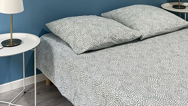 A bedroom with a blue wall, two circular woven wall decorations, a bed with a patterned bedspread, two bedside tables with lamps, and a round table with a lamp. - Apartment in the center of Castelnaudary (Castelnaudary)