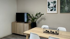 A modern dining area with a wooden table, white chairs, a black TV on a wooden cabinet, and two framed artworks on the wall. - Apartment in the center of Castelnaudary (Castelnaudary)