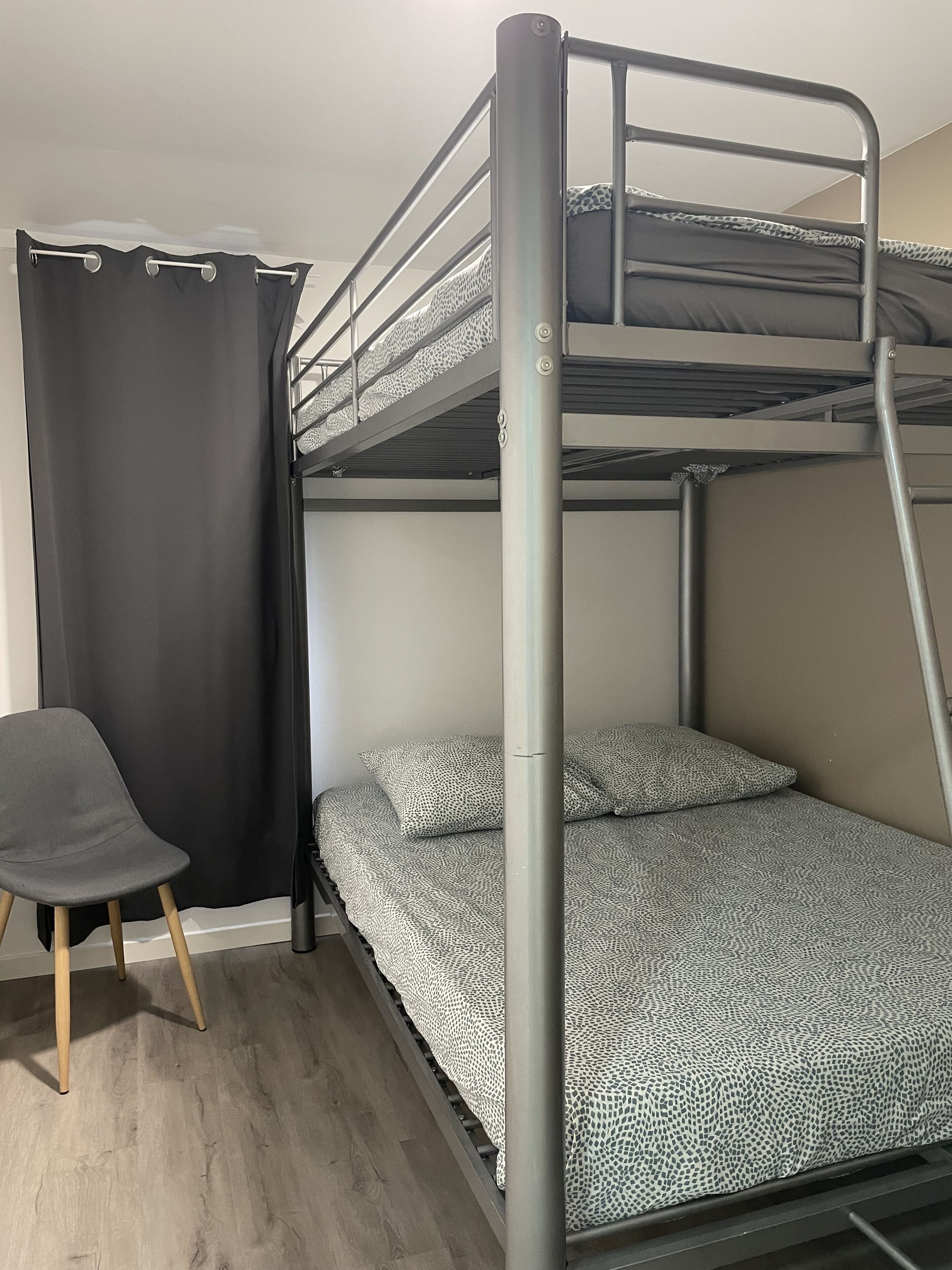 Un lit superposé avec une couvre-lit à motifs, une chaise et un rideau.