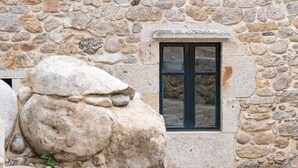 A stone building with a window and a large rock in the foreground. - A Palleira: Antiguo Pajar Reformado al Lado del río (Pobra do Caramiñal)