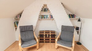 Eine gemütliche Leseecke mit zwei Sesseln, einer kleinen Holzkiste und Bücherregalen an einer weißen Ziegelwand.
