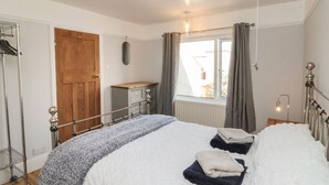 Ein Schlafzimmer mit einem Bett, einer Holztür, einem Fenster mit Vorhängen, einem Heizkörper und einem Metallregal.