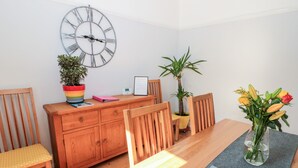 Ein Essbereich mit Holztisch, Stühlen, einer Uhr, Topfpflanzen und einer Blumenvase.