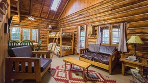A log cabin interior with a sofa, chairs, a small table, and a window with curtains. - Lakeside Cabin on Minerva Lake (Olmstedville)