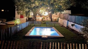 A rectangular pool with a wooden deck surrounding it, a wooden fence, and a tree with lights in the background. - Provencal villa 15 minutes from Cassis and the calanques (Gémenos)