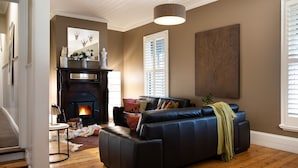 A cozy living room with a fireplace, leather sofa, and a large wall painting. - Maple Daylesford- quaint cottage with fireplace and spa (Daylesford)