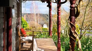A wooden bench with a red cushion on a wooden deck, surrounded by greenery and a red wooden structure.