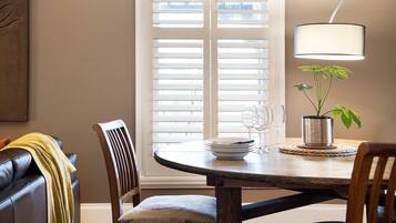 A dining area with a round wooden table, two chairs, a potted plant, and a table lamp.