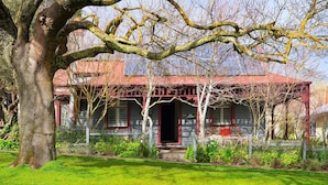 A house with a red roof, a porch with a bench, and a large tree in the foreground. - Maple Daylesford- quaint cottage with fireplace and spa (Daylesford)
