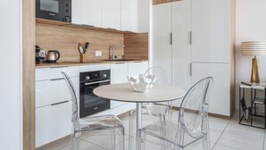 Een moderne keuken met witte kasten, een Bosch magnetron, een houten aanrecht en een ronde tafel met transparante stoelen.