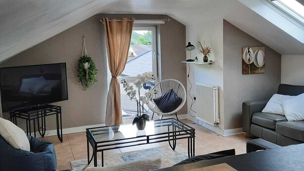 Una sala de estar moderna estilo loft, con una mesa de centro de vidrio, un sofá, un televisor sobre un mueble bajo y un tragaluz.