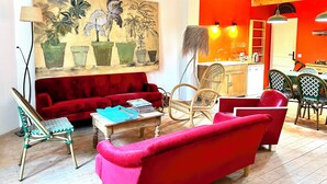 Een woonkamer met een rode bank, een houten salontafel en een schilderij van planten. Er is een keuken met een rode wand en houten kasten.