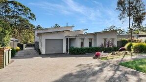 A two-story house with a garage, a covered driveway, and a well-maintained lawn with shrubs and flowers.