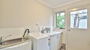 A compact kitchen with a sink, a white washing machine, and a window with a view of trees.