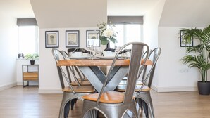 A dining area with a wooden table and metal chairs, framed artwork on the walls, and a potted plant. - Penthouse 23 (Newquay)