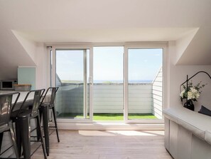 A modern kitchen with a dining area, large sliding glass doors to a balcony, and a view of the sky. - Penthouse 23 (Newquay)