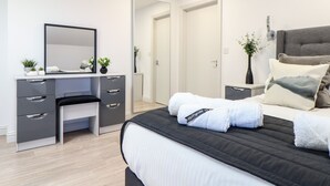 A modern bedroom with a bed, bedside table, and a desk with a mirror. - Penthouse 23 (Newquay)