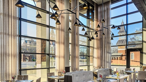 A restaurant with large windows, modern lighting, and a view of a historic building. - Laurel Hotel and Spa (Auburn)