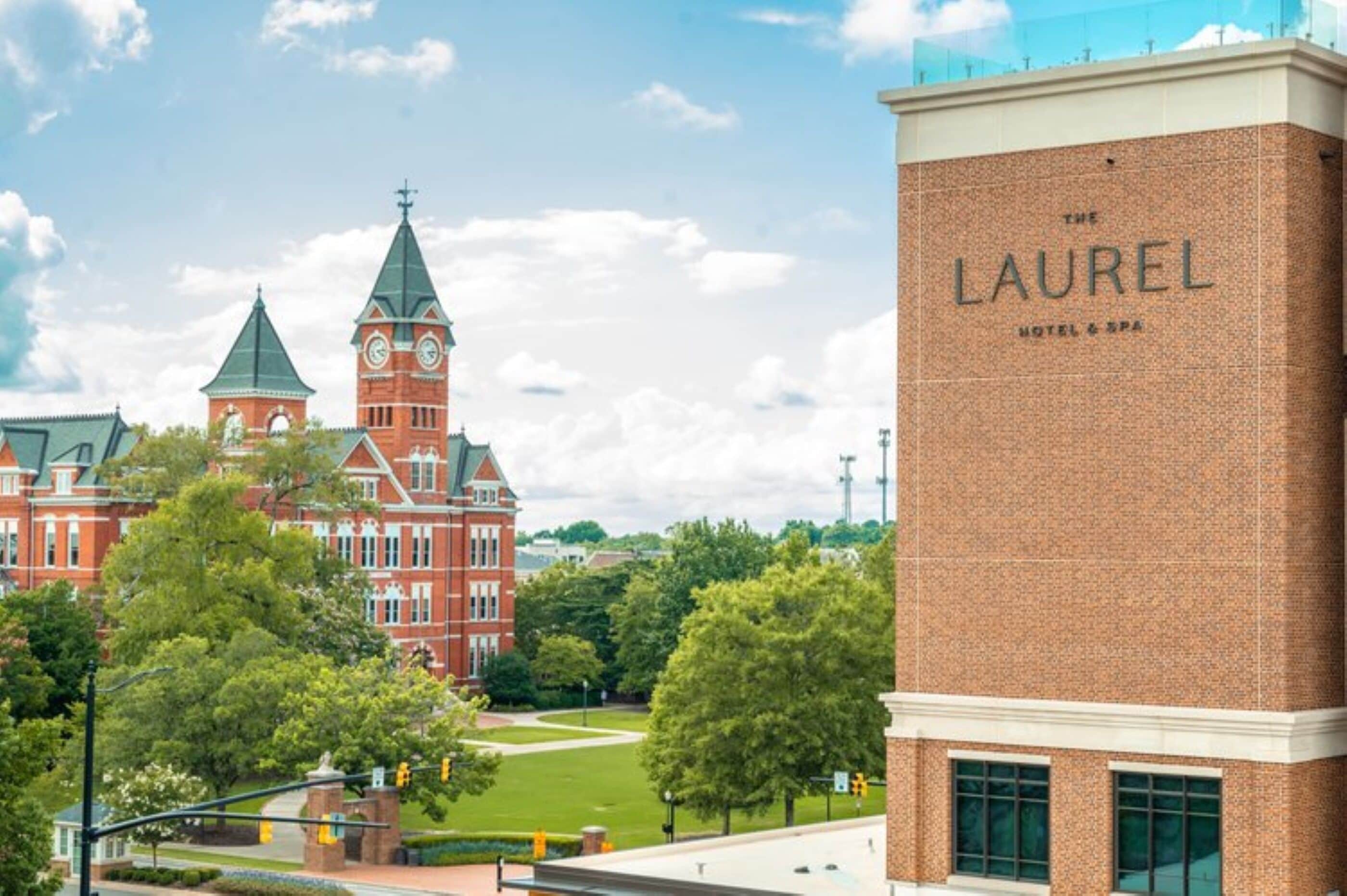 A red brick building with a clock tower and a modern hotel named "The Laurel Hotel & Spa" in the foreground.
