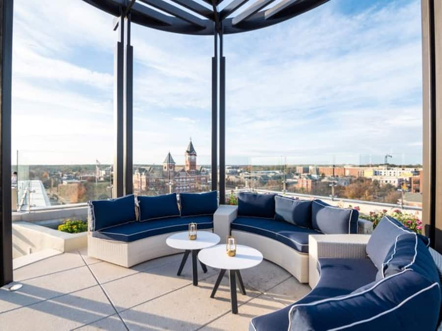 A rooftop terrace with a curved seating area, two small round tables, and a view of a cityscape including a clock tower.