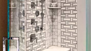 Un baño con pared de azulejos de diseño geométrico, cabina de ducha de vidrio, lavamanos de mármol y estante empotrado con artículos de aseo.