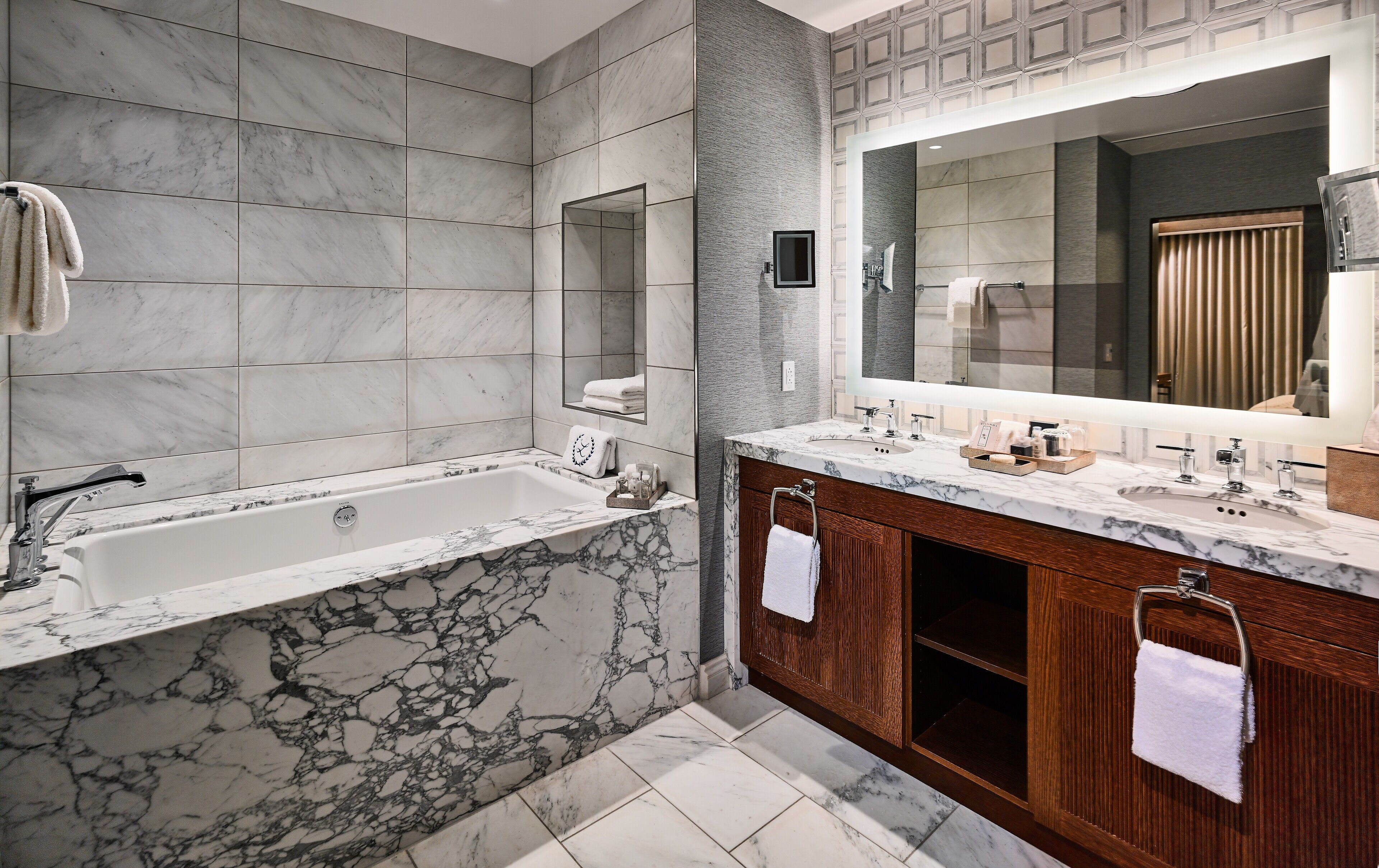 A modern bathroom with a marble bathtub, wooden vanity, and a large mirror.